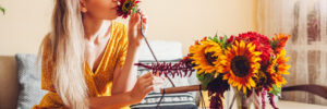 Woman smells sunflower arranging bouquet with red zinnia flowers in vase at home