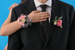 Young woman with corsage hugging her prom date on blue background, closeup