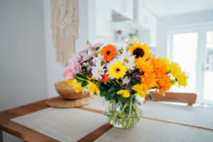 Kitchen counter table with focus on vase with huge multicolor various flower bouquet with blurred background of modern cozy white kitchen.