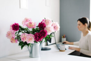 peonies in a garden watering can, on desktop in medical office. woman in the background