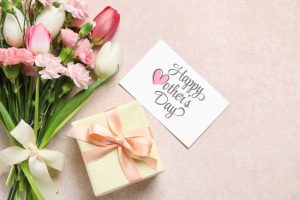 bouquet of different beautiful flowers with greeting card and gift box on beige background. mother's day celebration