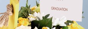 A beautiful bouquet filled with white and yellow flowers hangs against a soft blue background. a card proudly displays the words happy graduation, perfect for celebrating this special day.